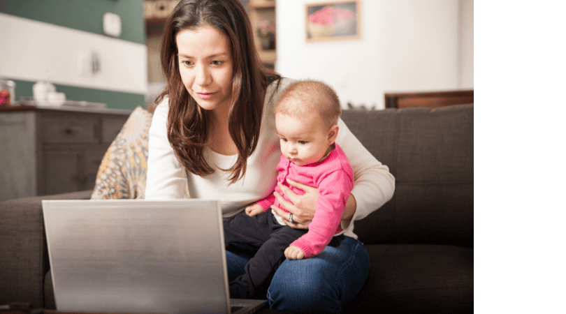 Lady holding baby whilst on laptop
